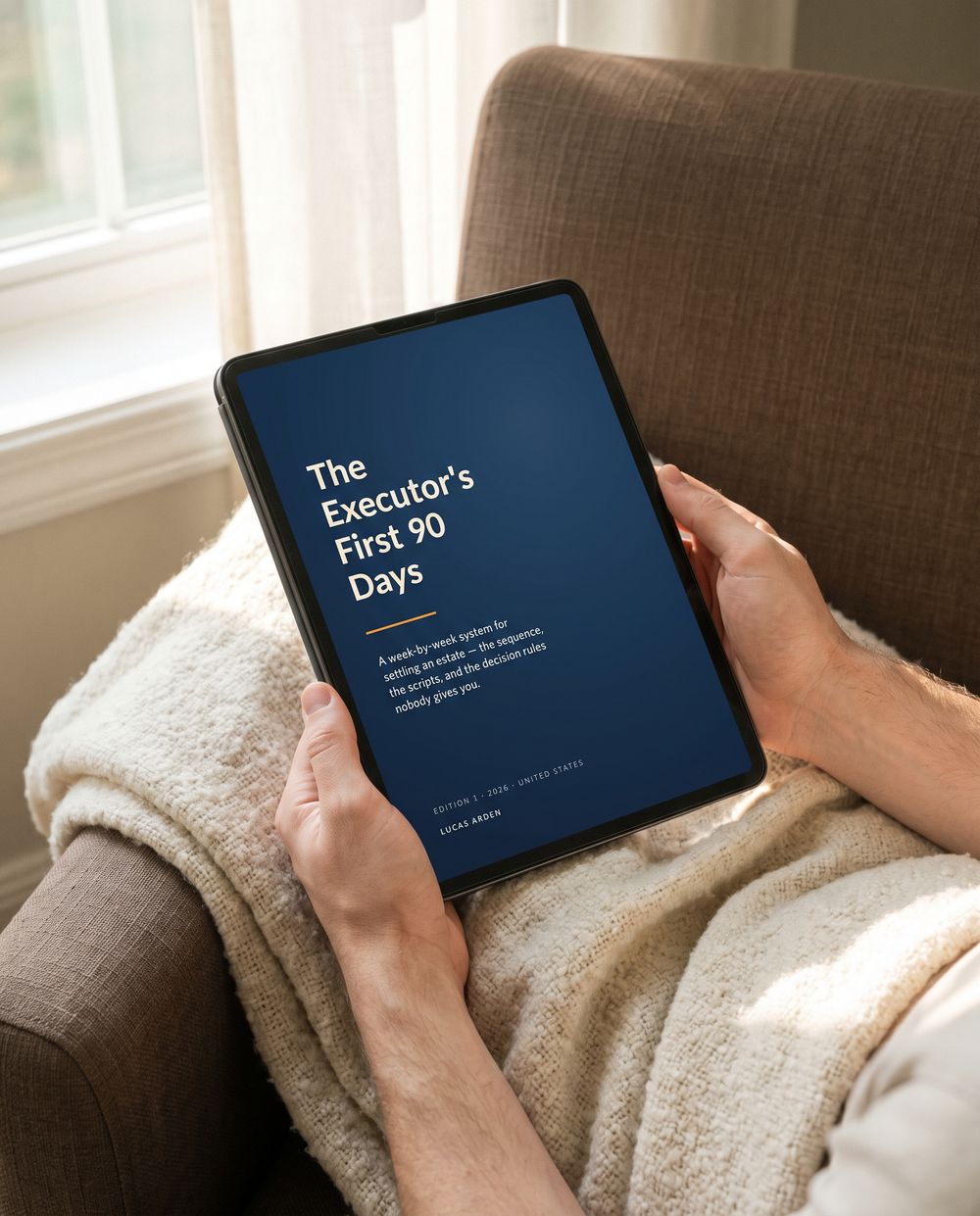 Hands holding a tablet showing the cover of The Executor's First 90 Days, in an armchair.